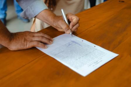 Person signing a legal will document in Ontario with a pen on a wooden table