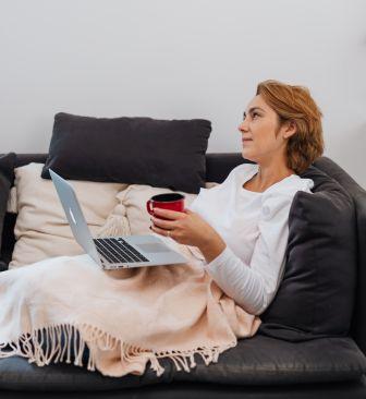 Canadian woman relaxing on couch with laptop and coffee completing her will kit online